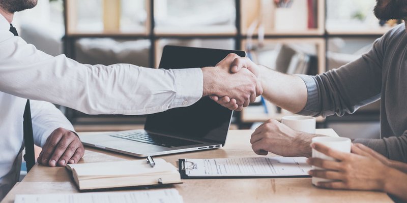 Two men shake hands over documents