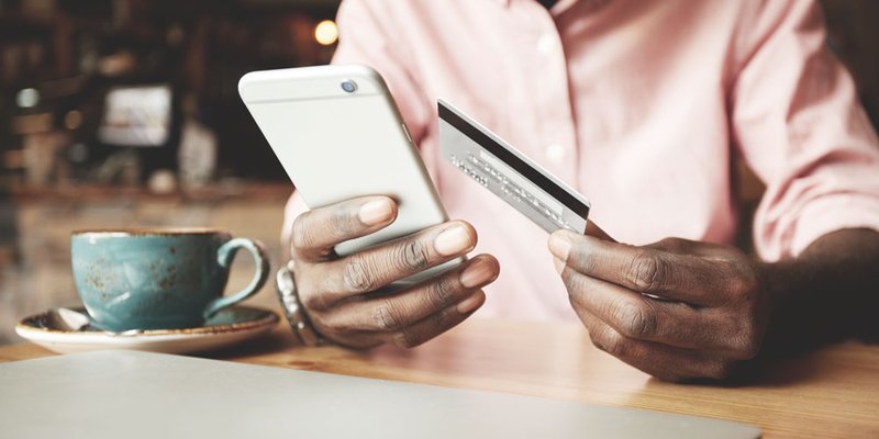 A close-up of a man holding his credit card and typing into his smartphone