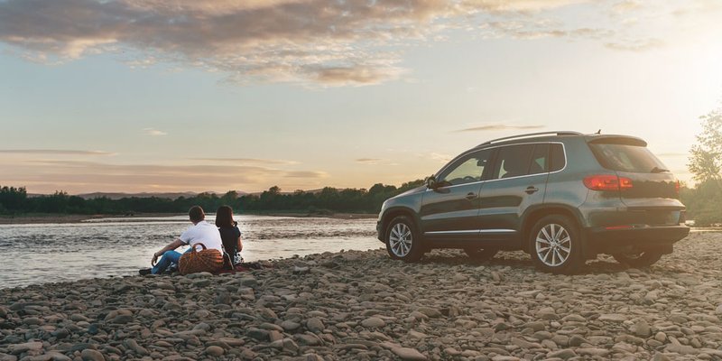 A couple sits on the edge of a riverbank a short distance away from their vehicle