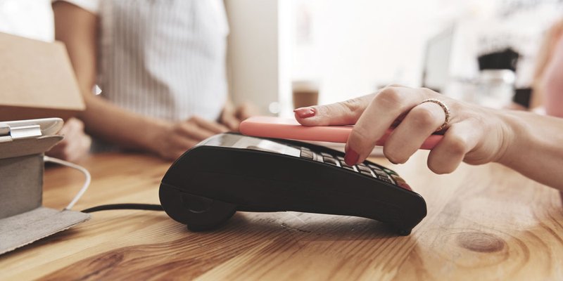 A hand with painted fingernails taps a smartphone on a point of sale terminal