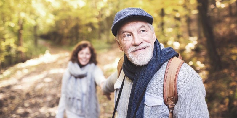 An older couple walk hand in hand in the woods