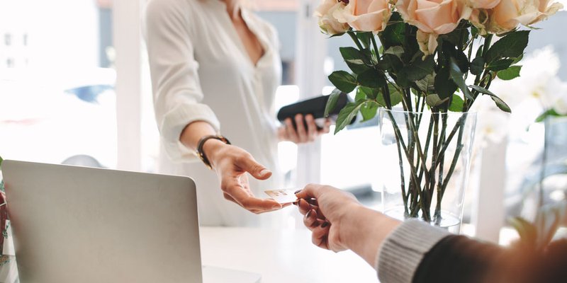 A woman hands her credit card to the employee at a flower shop