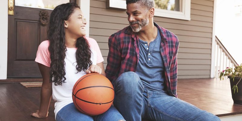 A dad sitting with his daughter who is holding a basketball