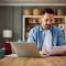 A concentrated adult man reading and analyzing a document while sitting in front of a laptop