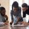 Focused African American millennial female team leader leaned over table, writing down project ideas, editing documentation at brainstorming business meeting with diverse partners or clients at office.