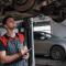 ar mechanic taking a look at car undercarriage and transmission while writing notes in a pad