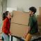 Happy couple carrying stacked cardboard boxes while moving into new apartment
