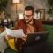 Man sitting at home and looking at laptop while hold a paper