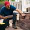 RepairmanWithTabletExaminingHomeExternalPorchWall