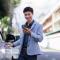 Young asian man smiling, using a smartphone app while opening a car door