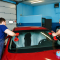 Two men replacing a windshield in a garage, wearing blue uniforms.