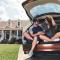 Couple sitting in the back of their car parked in their driveway in front of their home with a tablet smiling