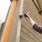 A woman paints the window frame exterior of a house