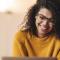 A happy young woman wearing a yellow sweater works on her laptop