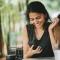A woman glances at and smiles at her phone while waiting for a friend at a cafe
