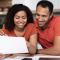 Smiling millennial african american wife and husband in same t-shirts work with documents, calculate profit in kitchen interior