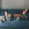 Woman laying on her couch in small urban apartment on her laptop