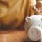 A person drops a coin into a piggy bank while sitting at a table with a coffee