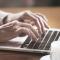 A close-up of an older person typing on the computer