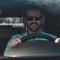 A male driver wears sunglasses in the driver's seat of a car