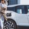 A woman leans against her electric vehicle while it charges