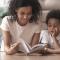A mother lays on the floor and reads to her child