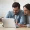 A couple lean in to look at something on a laptop