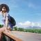 A woman wearing a sun hat sits on a railing with a mountain view