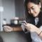 A young woman sits on a couch and shops using her phone and a credit card