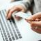 Hands are seen holding a credit card and typing numbers into a laptop computer