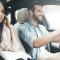 A male driver sits smiling with a female passenger on a bright day