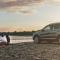 A couple sits on the edge of a riverbank a short distance away from their vehicle